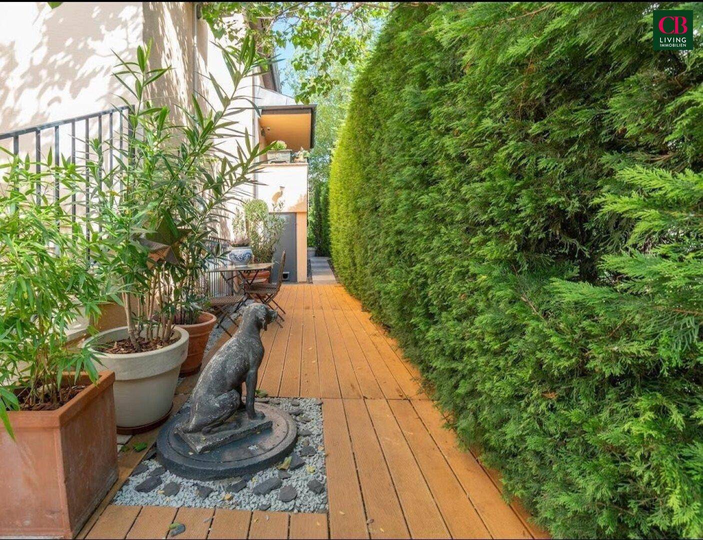 Schmaler Gartenweg aus Holzplanken, gesäumt von hohen Hecken und Topfpflanzen.