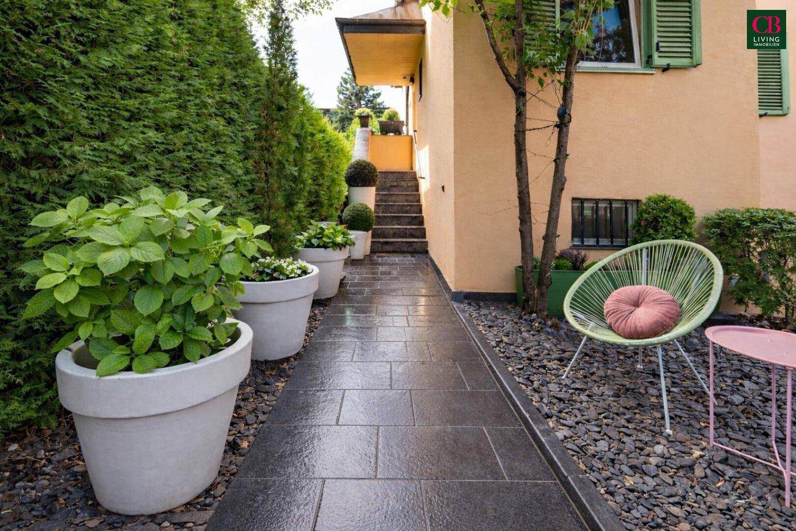 Moderner Gartenweg aus dunklen Fliesen, umgeben von Kies und großen Pflanzkübeln.