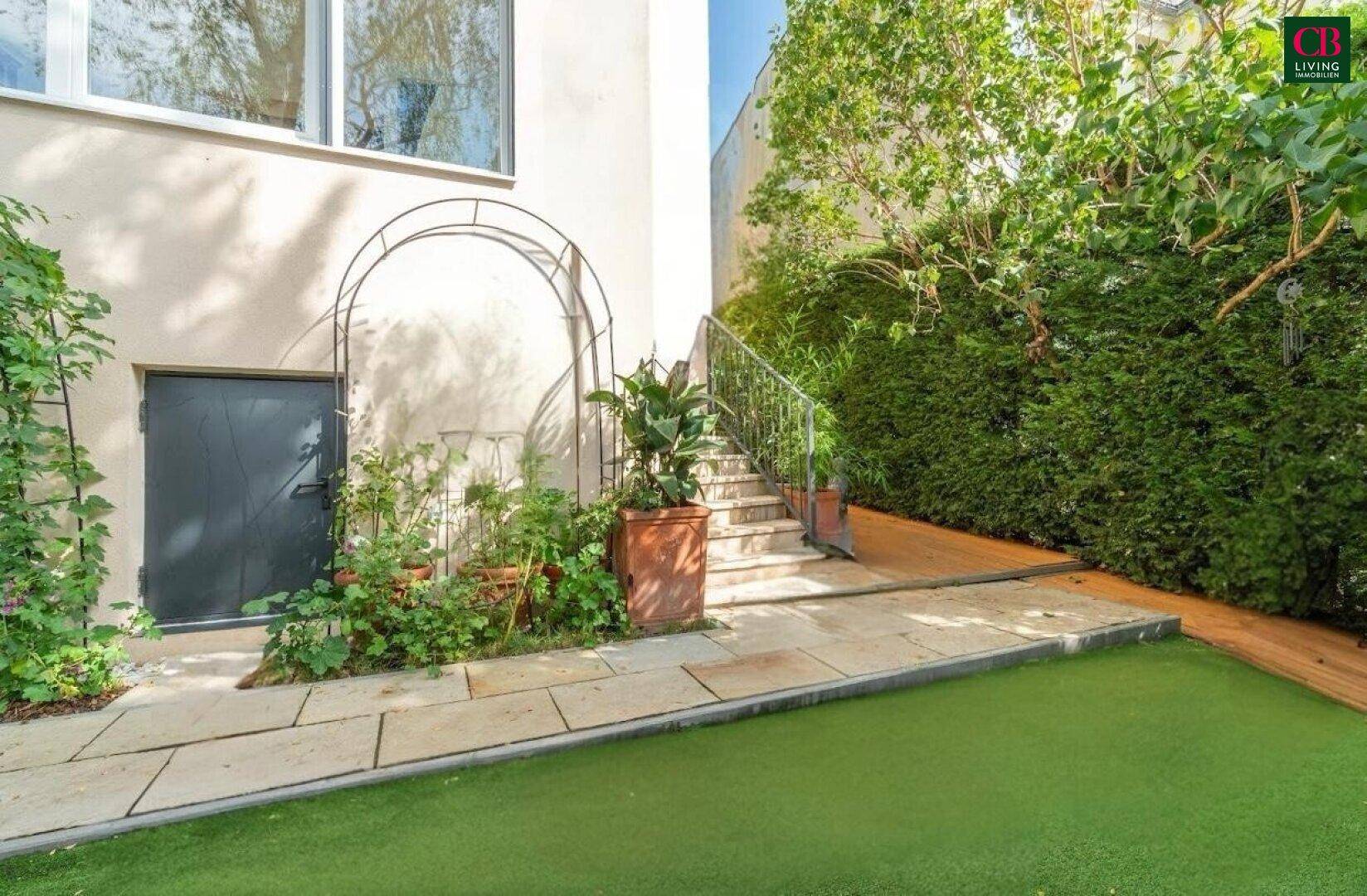 Gartenbereich mit Kunstrasen, Steinfliesen und einer Treppe, die zum oberen Bereich führt.