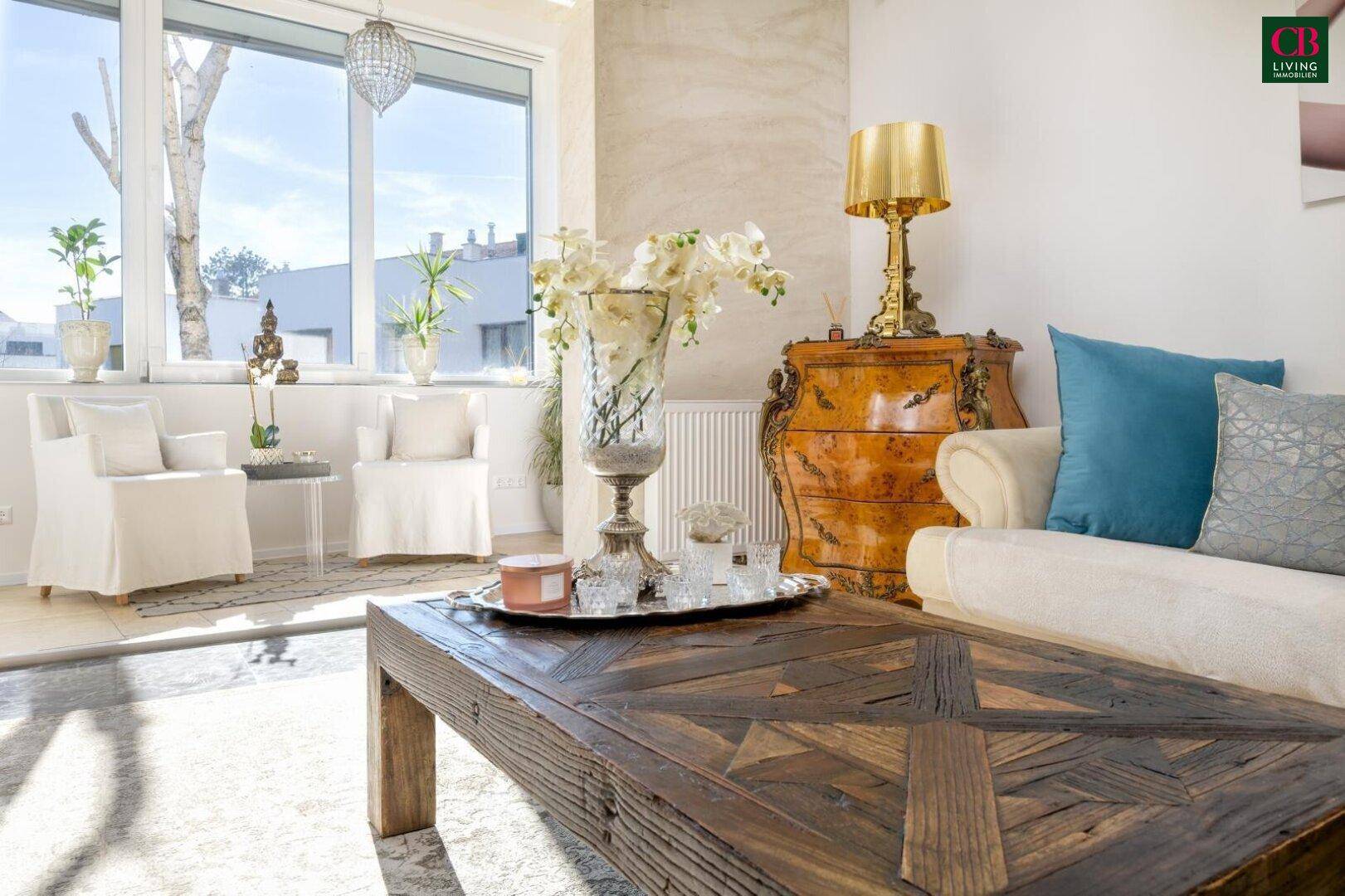 Gemütlicher Wohnbereich mit Holztisch, Blumenarrangement und Blick auf den sonnigen Außenbereich.