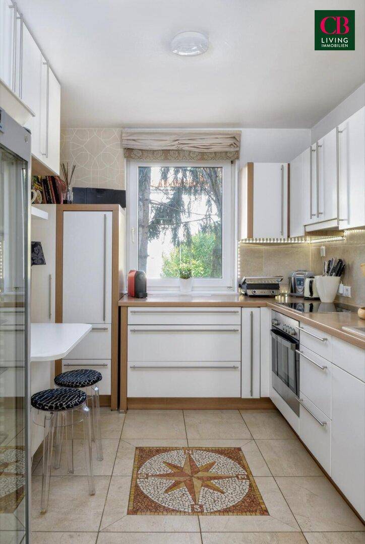 Funktionale Küche mit weißen Schränken, Fliesenboden und Fenster mit Blick ins Grüne.