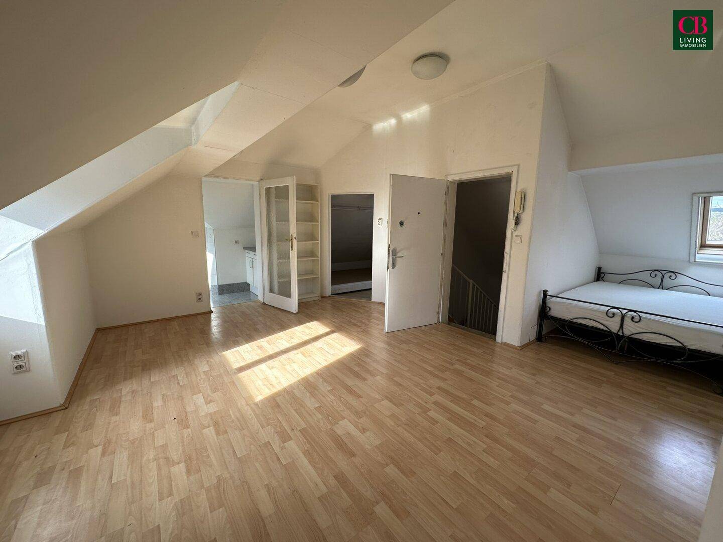 Dachgeschosszimmer mit schrägen Wänden, Laminatboden und einem Bettgestell.