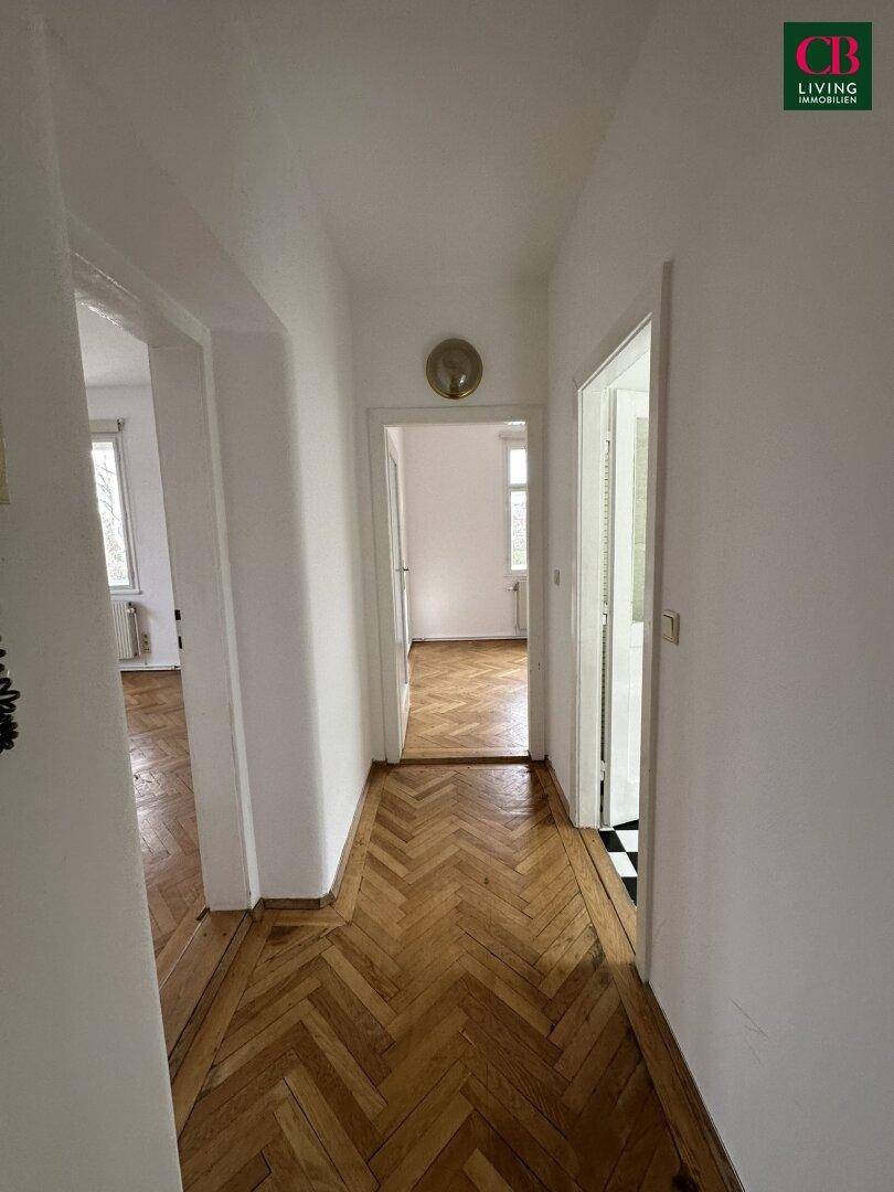 Langer Flur mit klassischem Fischgrätparkett und weißen Wänden.