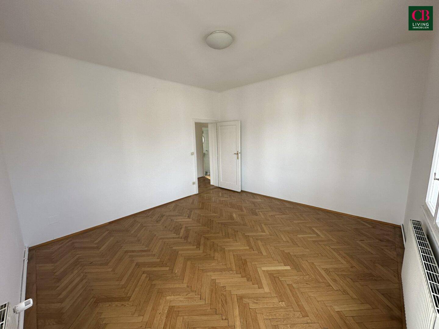 Helles, unmöbliertes Zimmer mit Parkettboden und schräger Wand.