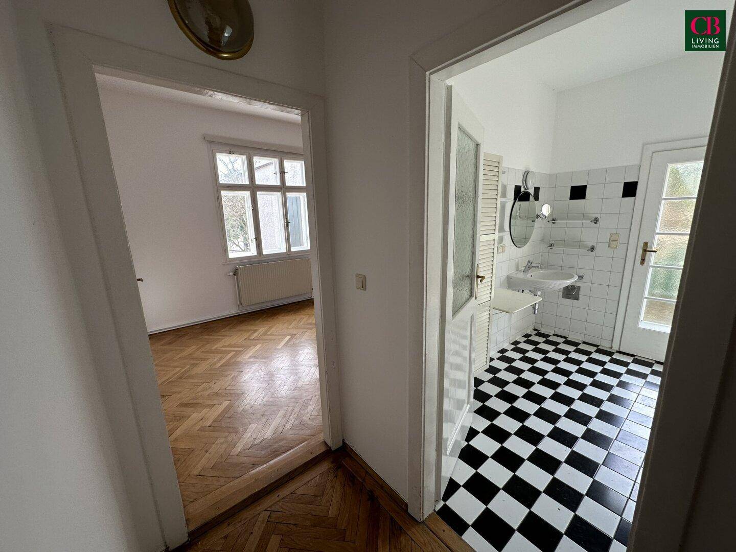 Flur mit Blick in ein Zimmer und ein Badezimmer mit schwarz-weißem Fliesenboden.