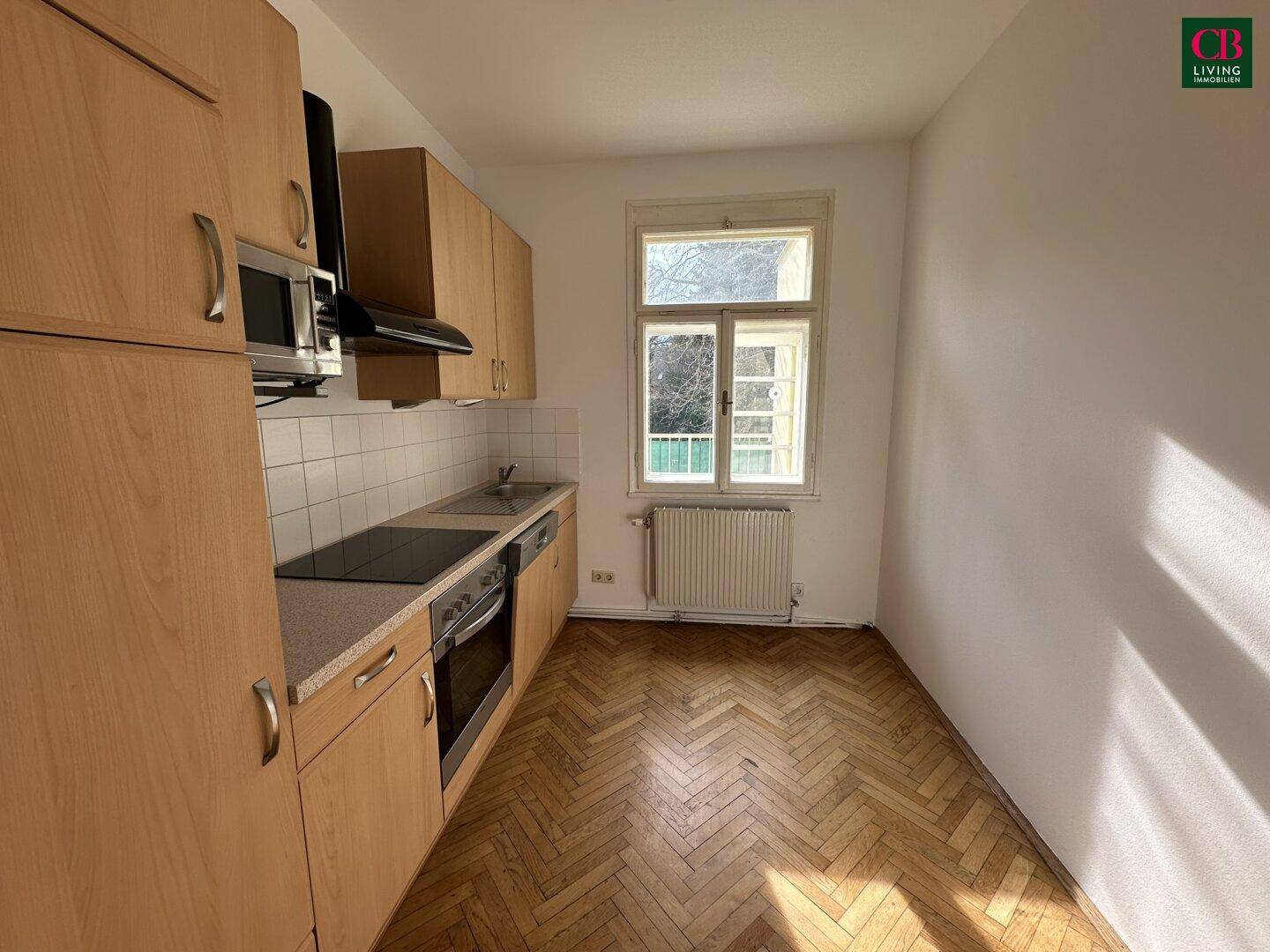 Ältere Küche mit Holzschränken, Einbaugeräten und Fischgrätparkett.
