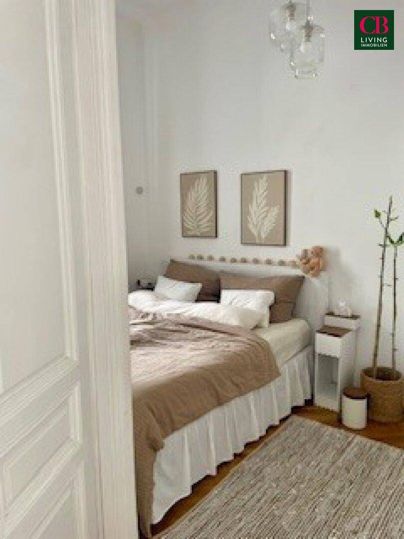 Gemütliches Schlafzimmer mit Doppelbett, schlichter Dekoration und hellem Holzboden, durch eine Tür sichtbar.