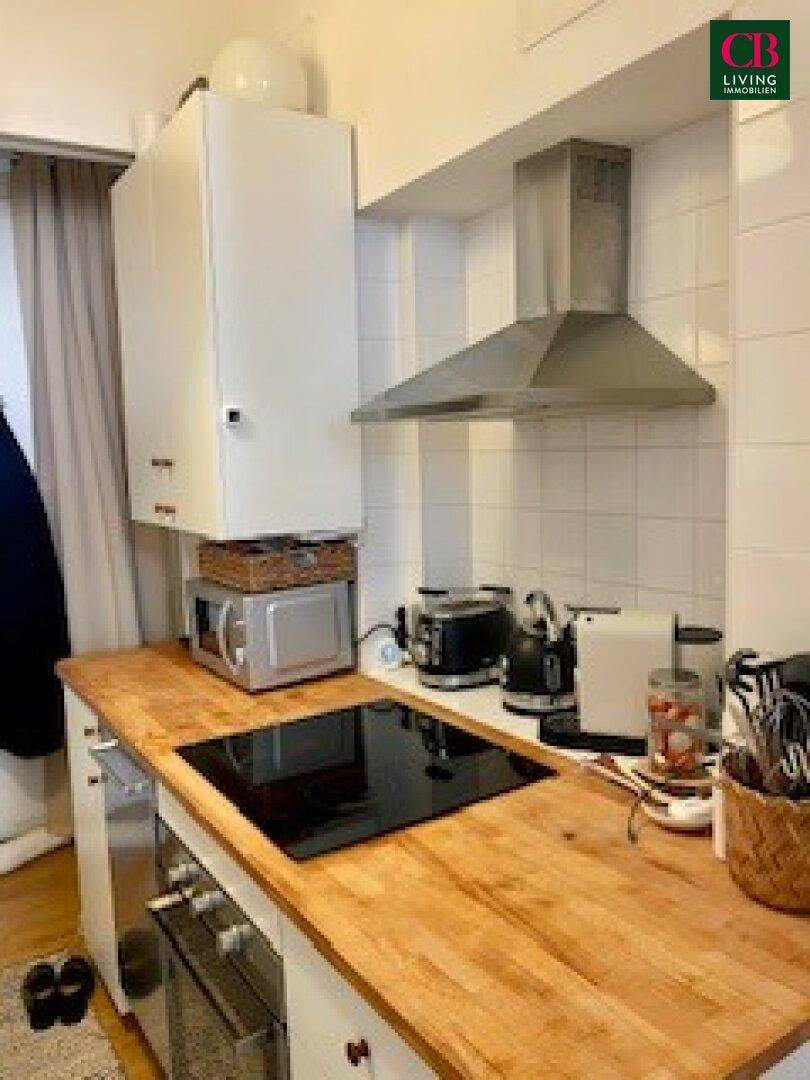 Kompakte Küche mit Holzarbeitsplatte, weißen Schränken, Induktionskochfeld und Dunstabzugshaube.