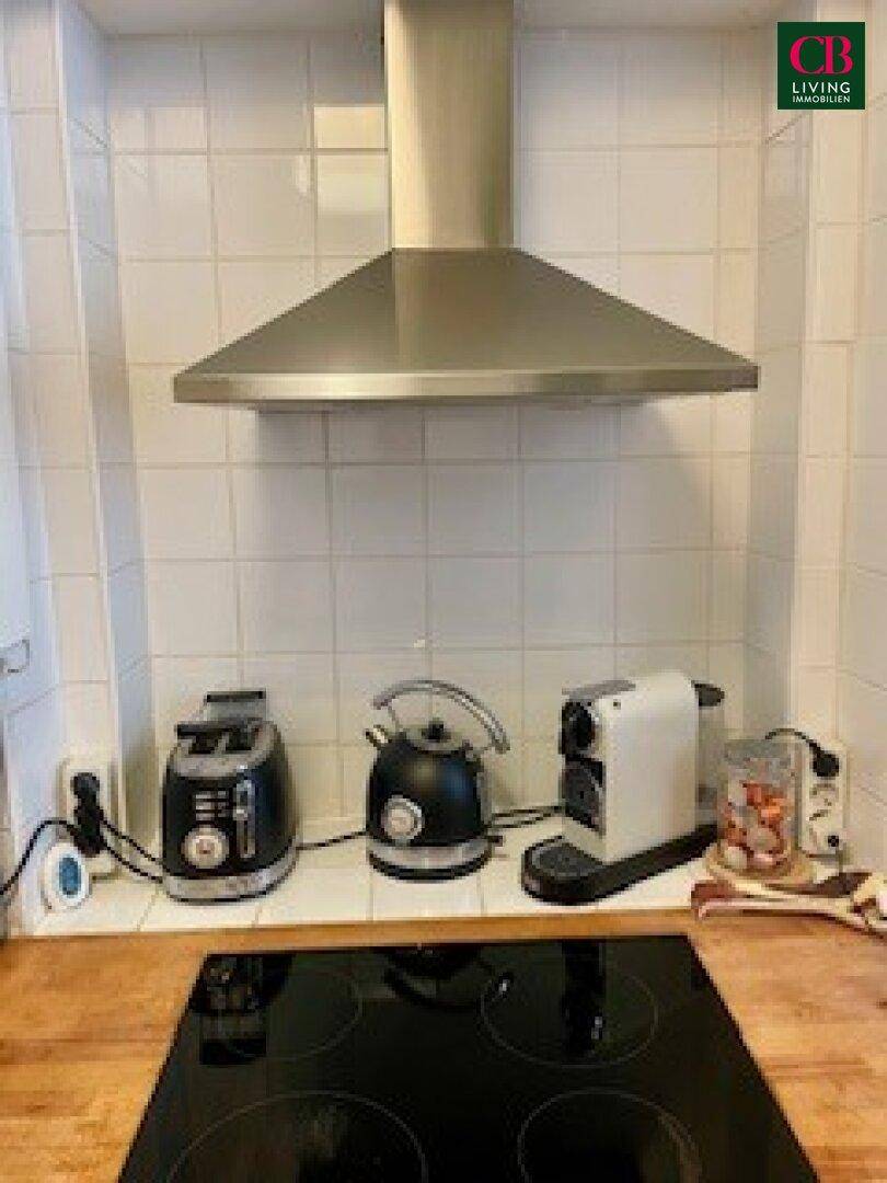 Detailansicht der Küche mit Induktionskochfeld, Dunstabzugshaube und verschiedenen Küchengeräten auf der Holzplatte.