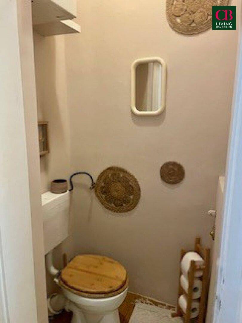 Kleines Gäste-WC mit beigen Wänden, einem Holz-Toilettensitz und minimalistischer Einrichtung.