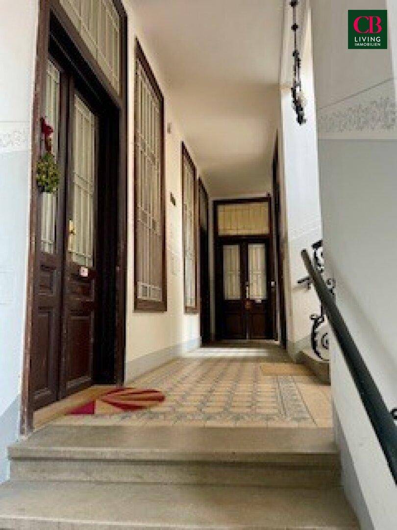 Langer Flur im Altbau mit gemustertem Fliesenboden, hohen Decken und klassischen Holztüren.