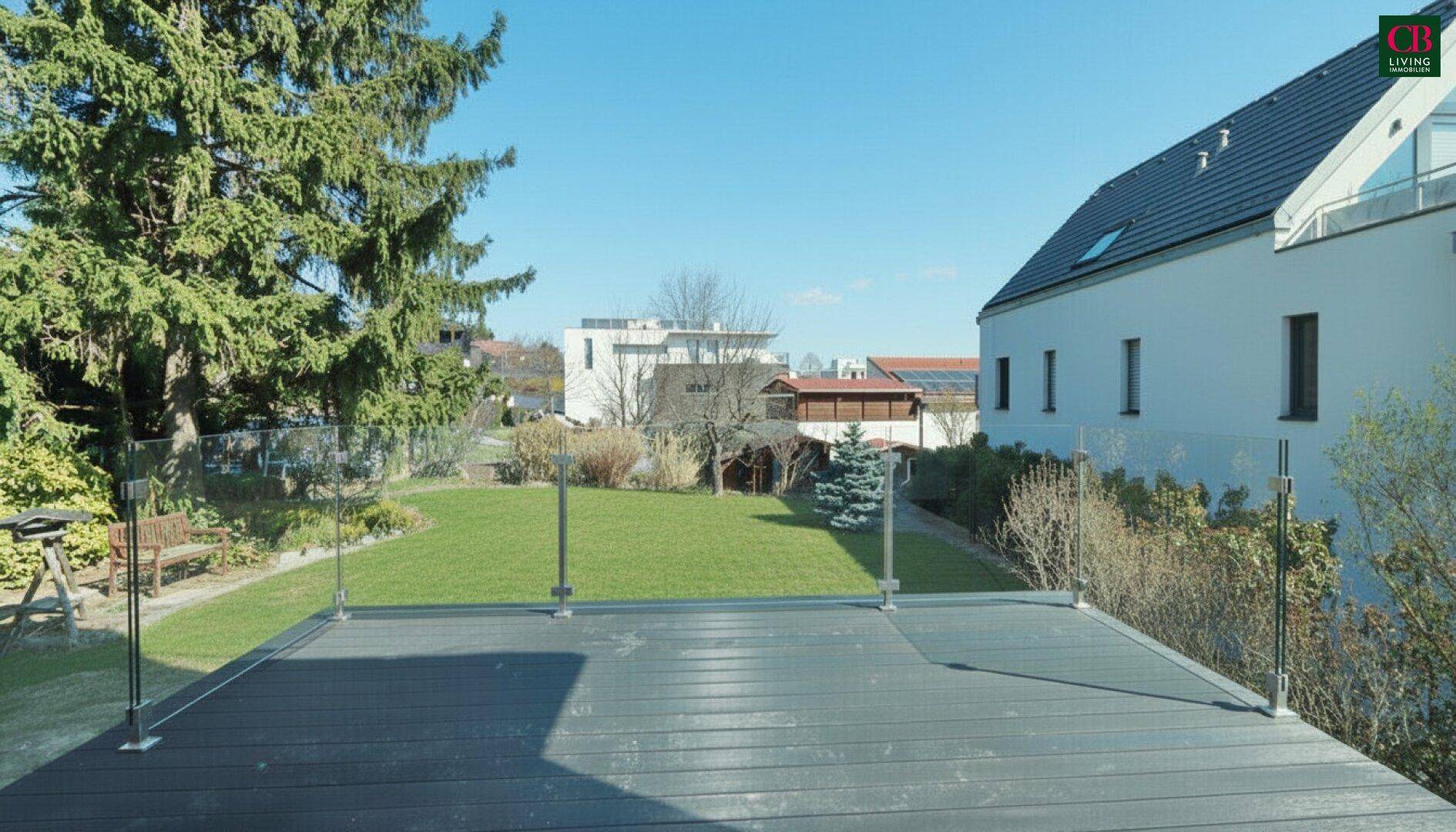 Moderne Terrasse mit Glasgeländer und dunklem Bodenbelag, mit Blick auf den Garten.