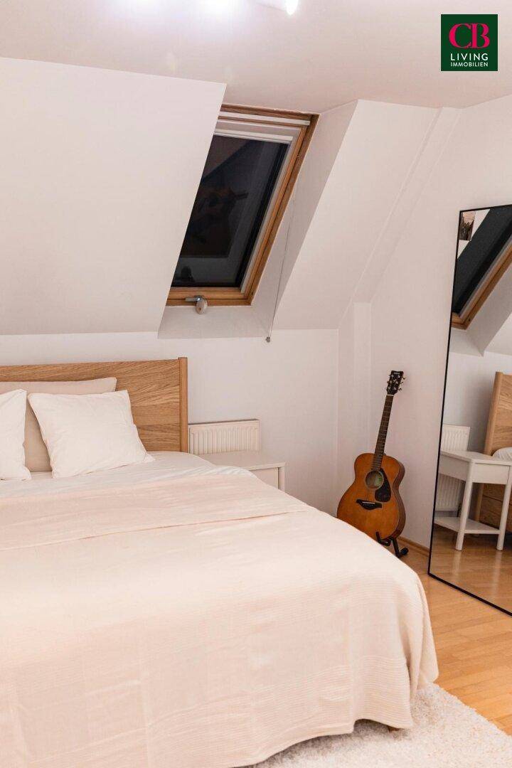 Helles Schlafzimmer mit Holzbett, Dachschräge und Dachfenster, das viel Licht hereinlässt.