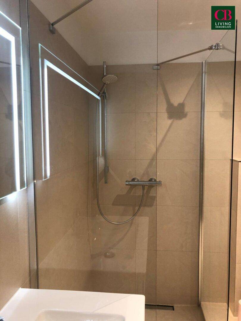 Detailansicht der modernen, begehbaren Dusche mit Regenduschkopf und Glasabtrennung.