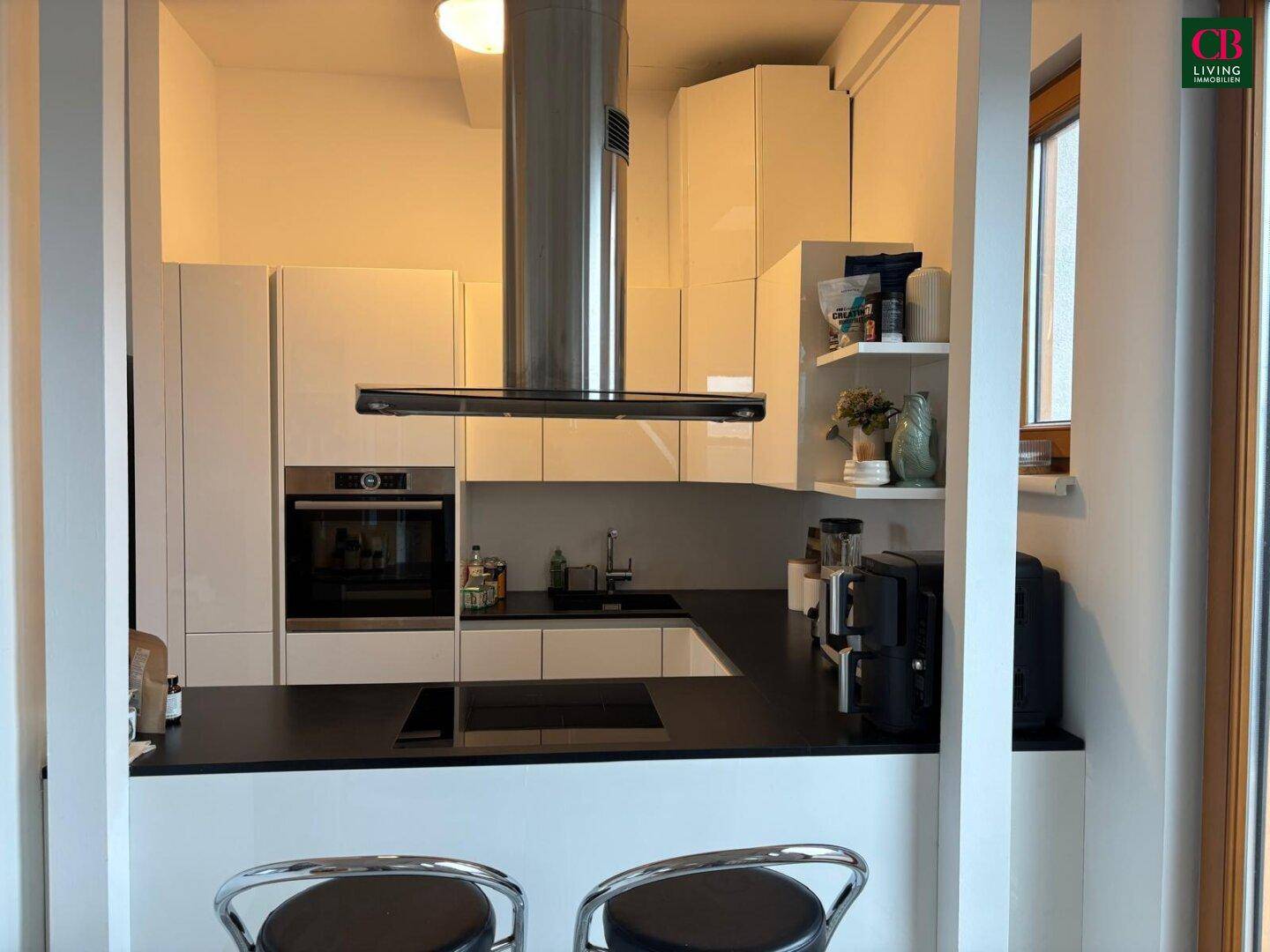 Moderne Küche mit weißen Hochglanzfronten, dunkler Arbeitsplatte und integrierten Geräten sowie einer Frühstücksbar.