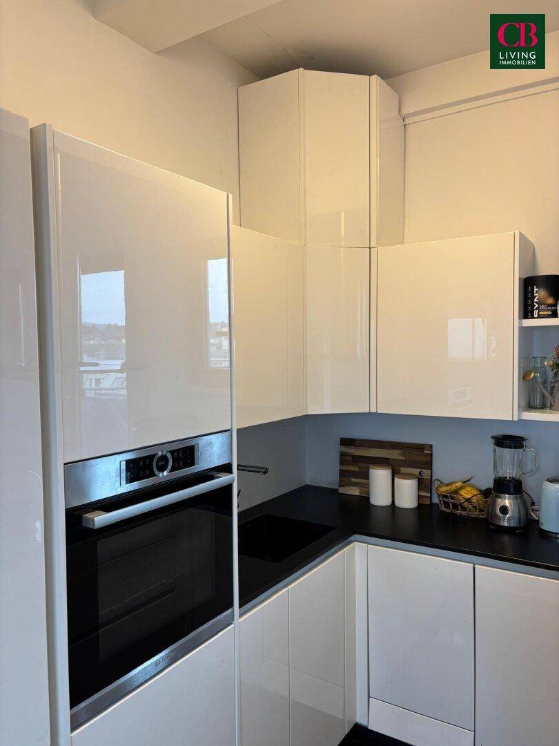 Moderne Einbauküche mit glänzenden weißen Fronten, dunkler Arbeitsplatte und integriertem Backofen.