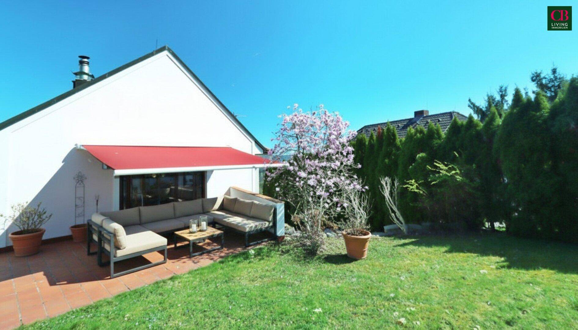 Geräumige Terrasse mit bequemen Gartenmöbeln und angrenzendem Rasenbereich unter blauem Himmel.