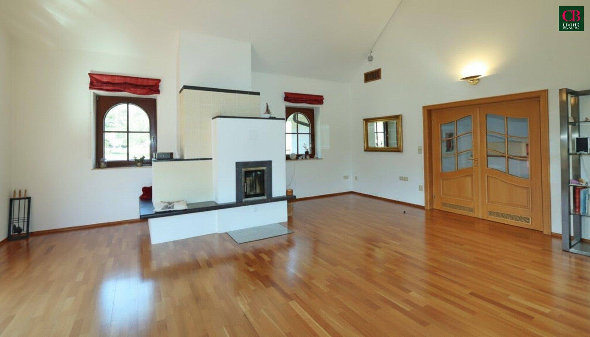 Großes Wohnzimmer mit Holzboden, Kamin und doppelter Holztür zum Flur.