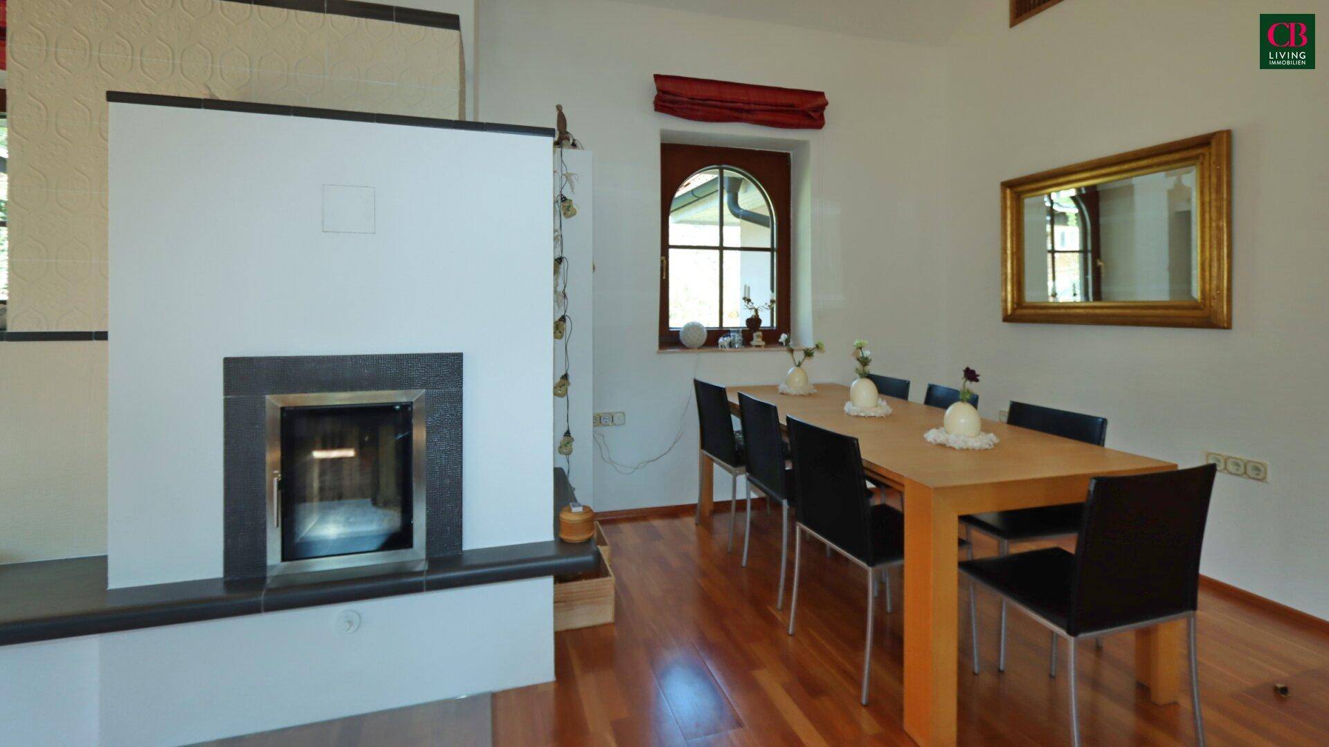 Essbereich mit Holztisch, schwarzen Stühlen und Kamin, angrenzend an den Wohnbereich.