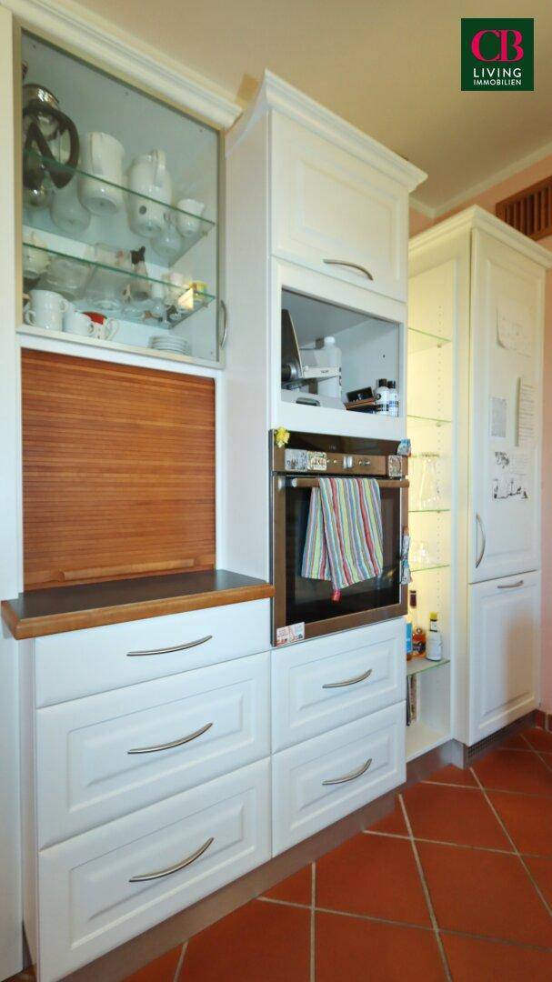 Detailansicht der weißen Einbauküche mit integriertem Backofen und Holzrollladen.