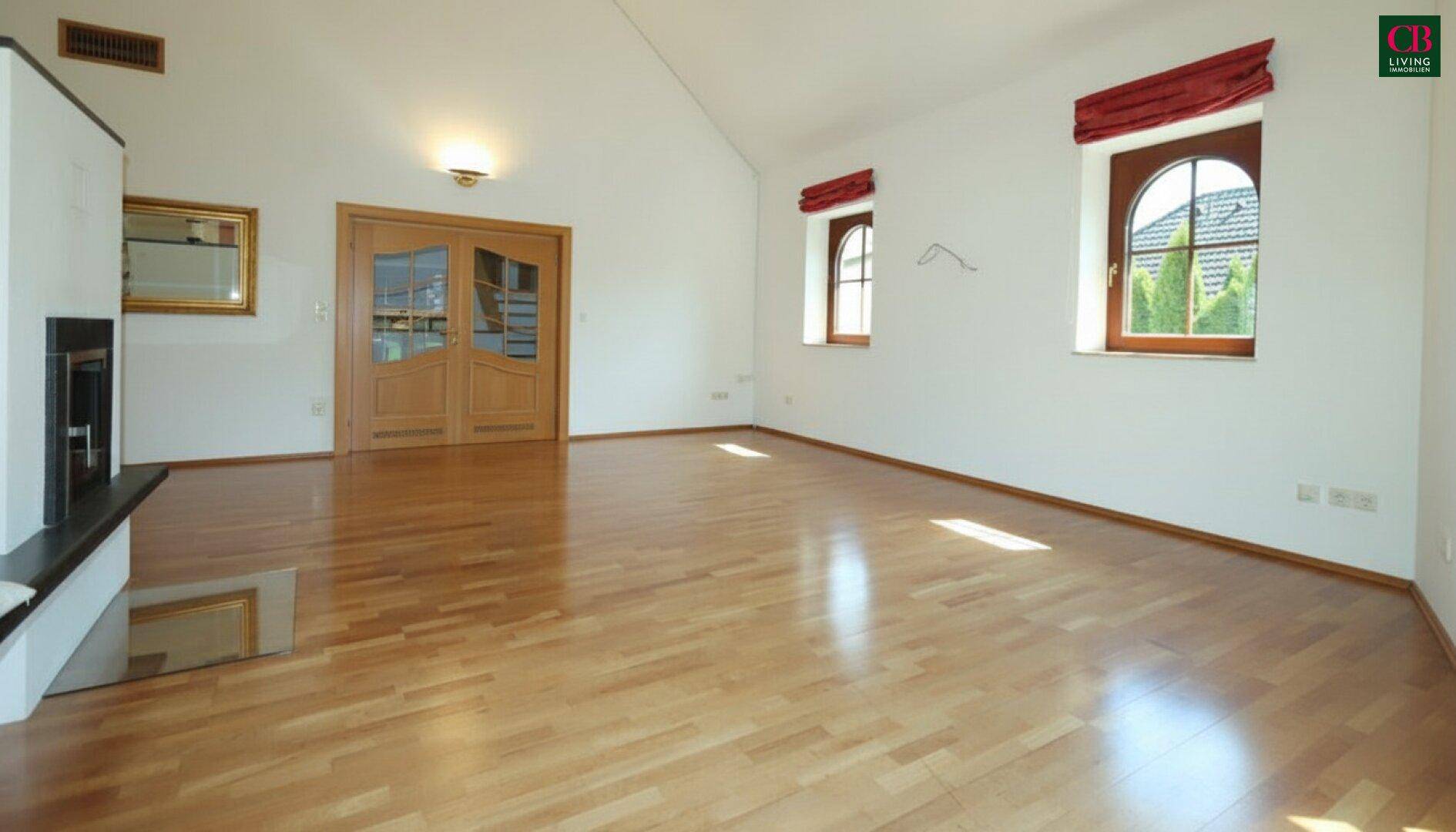 Heller Wohnbereich mit Holzboden, Kamin und doppelter Holztür, die zum Flur führt.