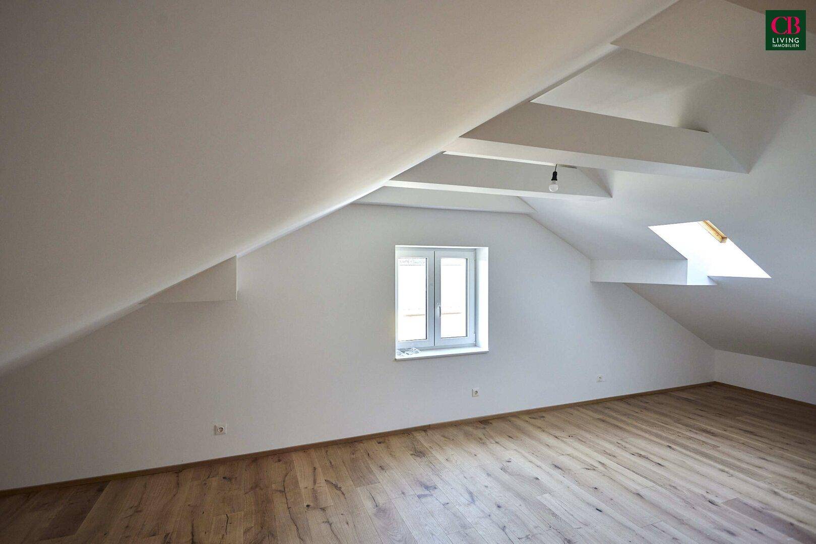 Helles Dachgeschosszimmer mit schrägen Wänden, Holzboden und einem zusätzlichen Dachfenster.