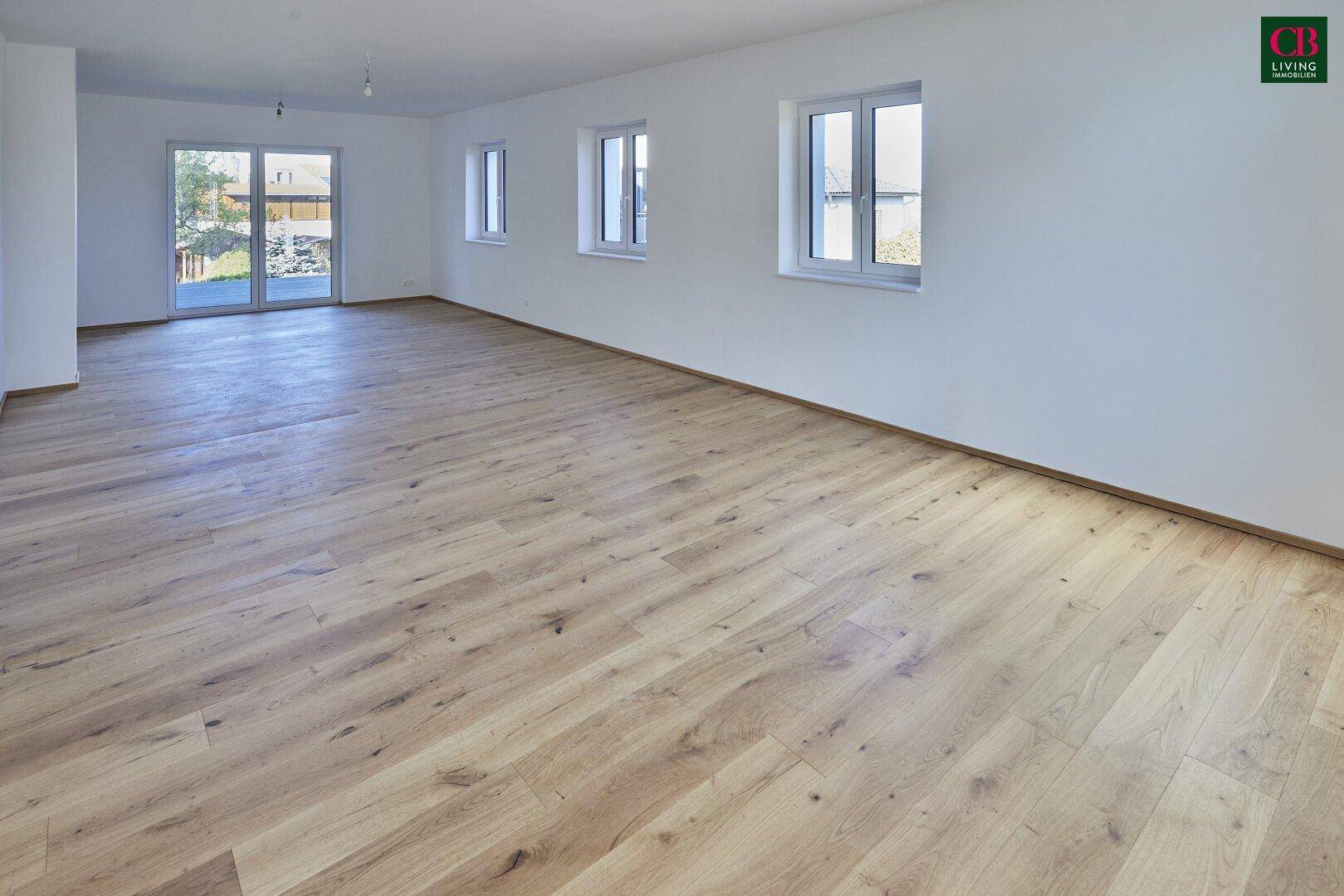 Heller Raum mit Holzboden und großer Glasschiebetür, die Zugang zum Außenbereich bietet.