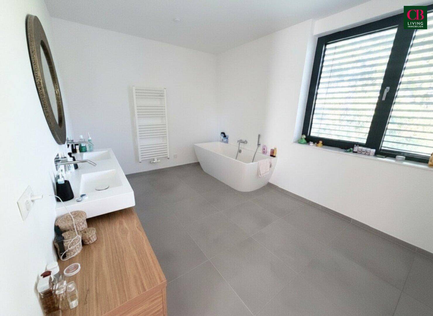 Helles Badezimmer mit freistehender Badewanne, Doppelwaschbecken und beheiztem Handtuchhalter.