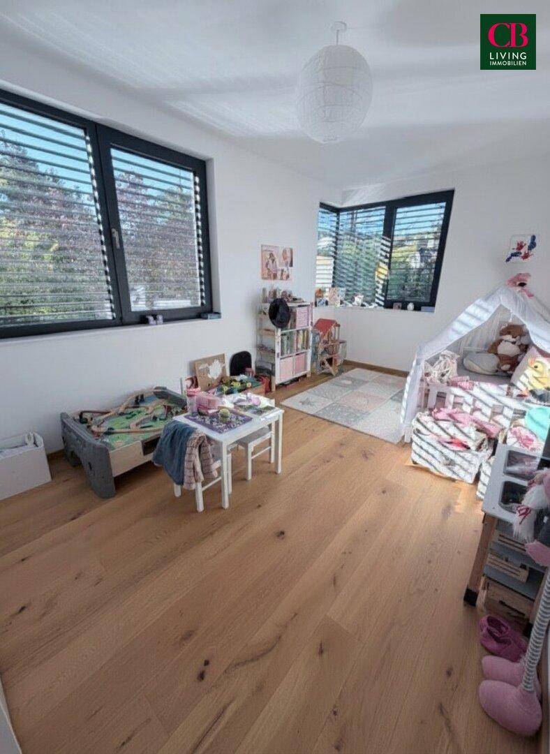 Helles Kinderzimmer mit Holzboden, großen Fenstern und kindgerechter Einrichtung.