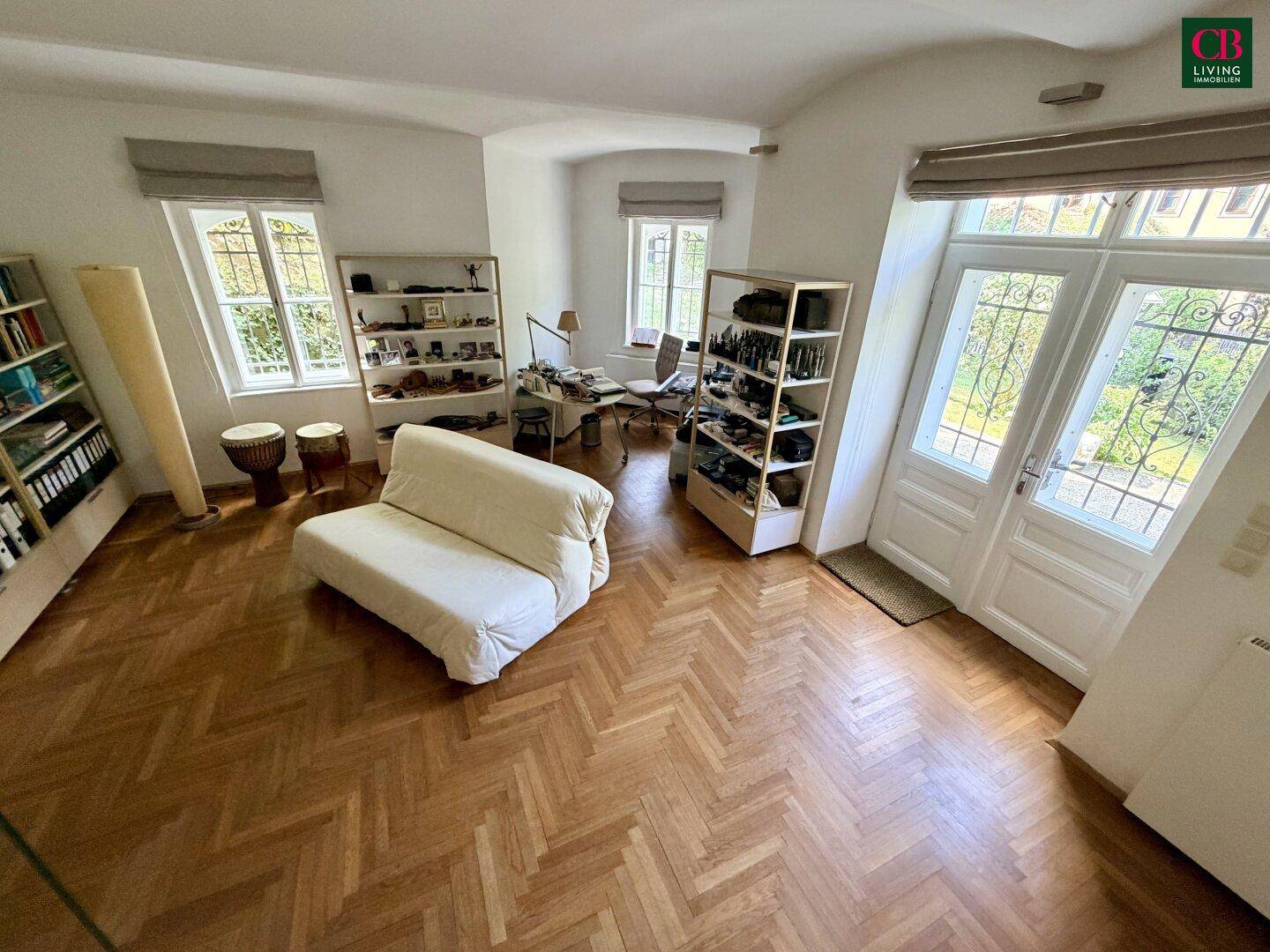 Helles Arbeitszimmer mit Fischgrätparkett, Regalen und Zugang zu einem Außenbereich durch Flügeltüren.