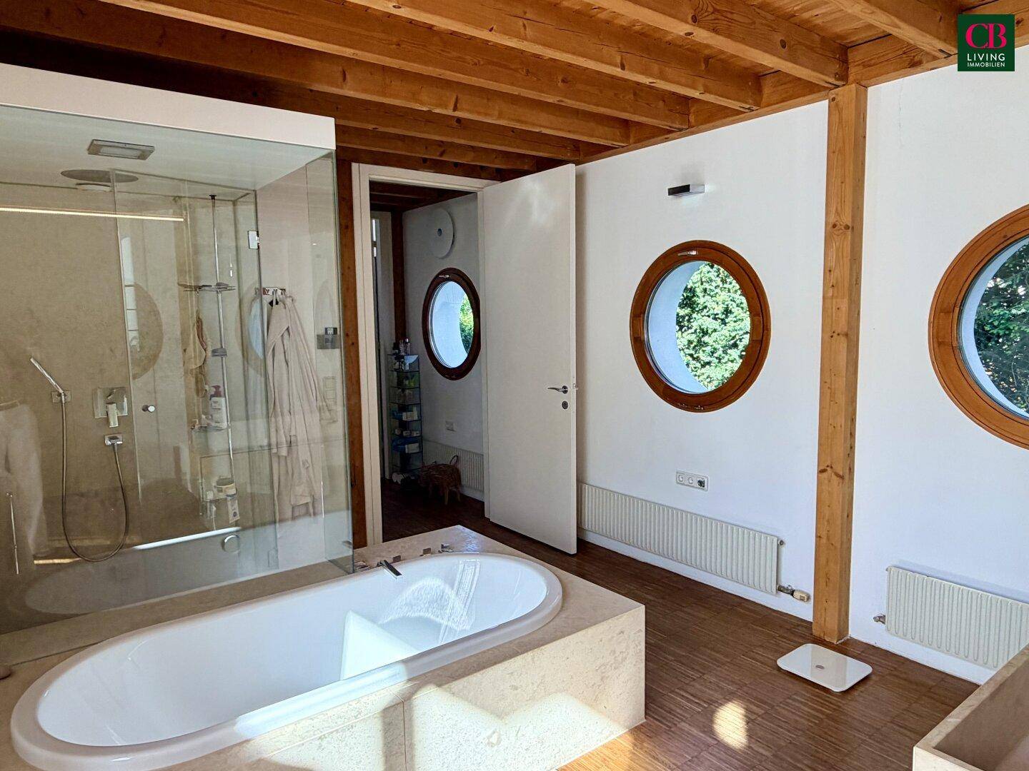 Helles Badezimmer mit Badewanne, begehbarer Dusche und runden Fenstern, die viel Licht hereinlassen.