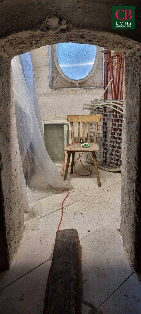 Rustikaler Abstellraum mit gewölbtem Eingang, einem runden Fenster und verschiedenen Utensilien.