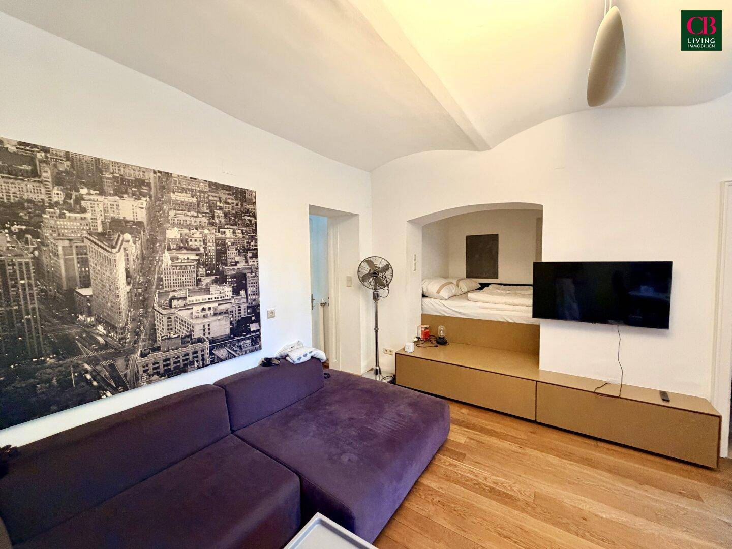 Wohnzimmer mit gemütlicher Sitzecke und integriertem Schlafbereich in einer Nische, modern eingerichtet.