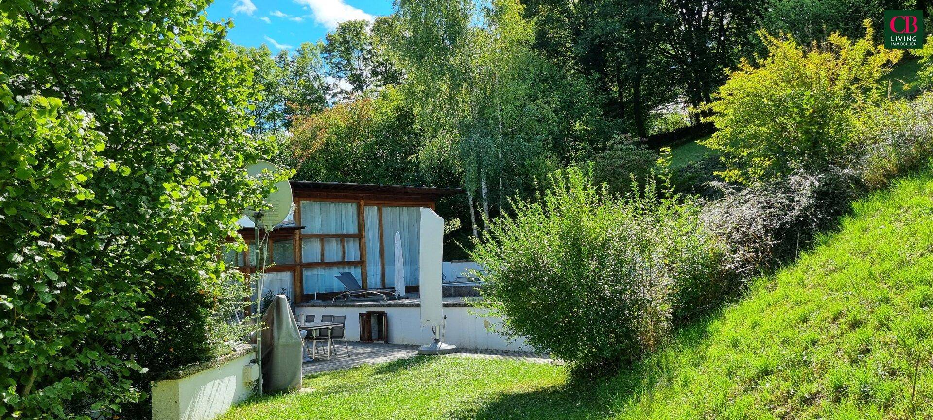 Gepflegter Gartenbereich mit Rasenfläche und üppiger Bepflanzung, angrenzend an eine Terrasse.