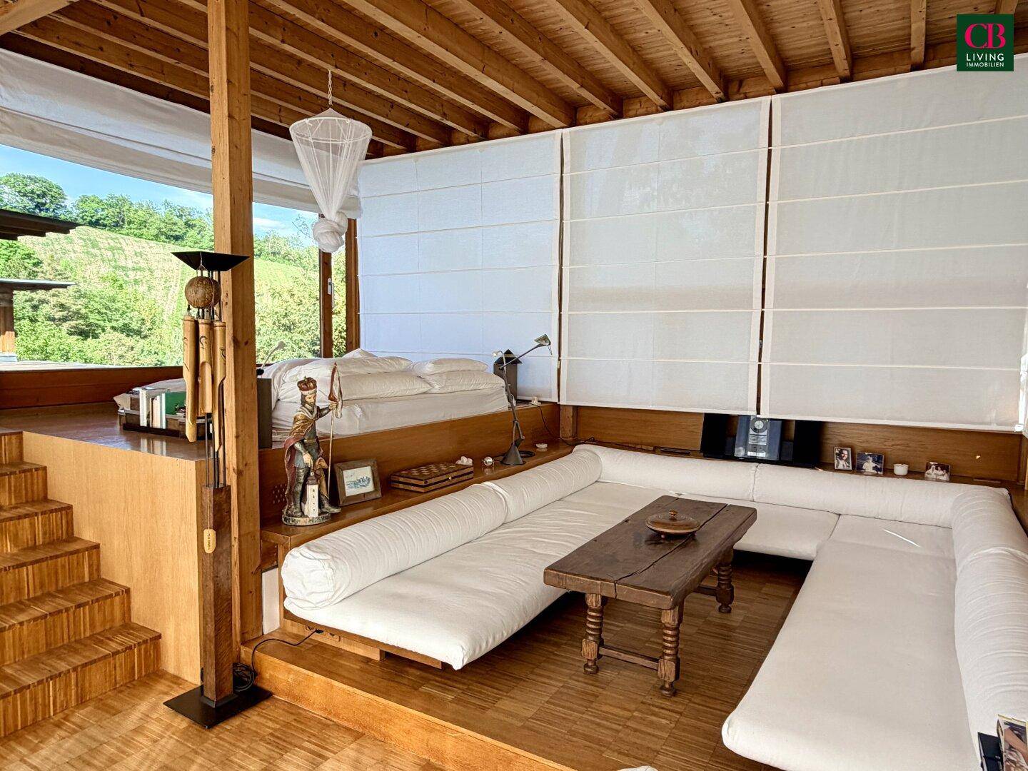 Gemütlicher Wohnbereich mit niedrigen Sofas, Holzboden und Holzdecke, umgeben von großen Fenstern.