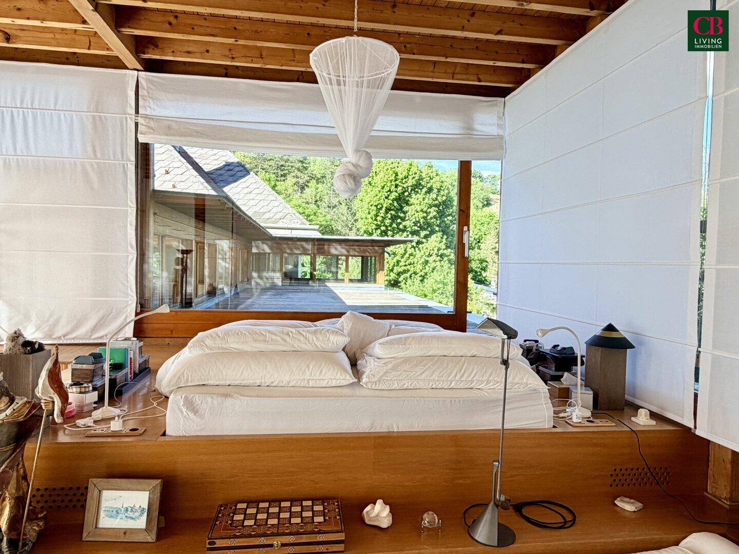Schlafzimmer mit großem Bett und bodentiefen Fenstern, die einen weiten Blick in die Natur bieten.