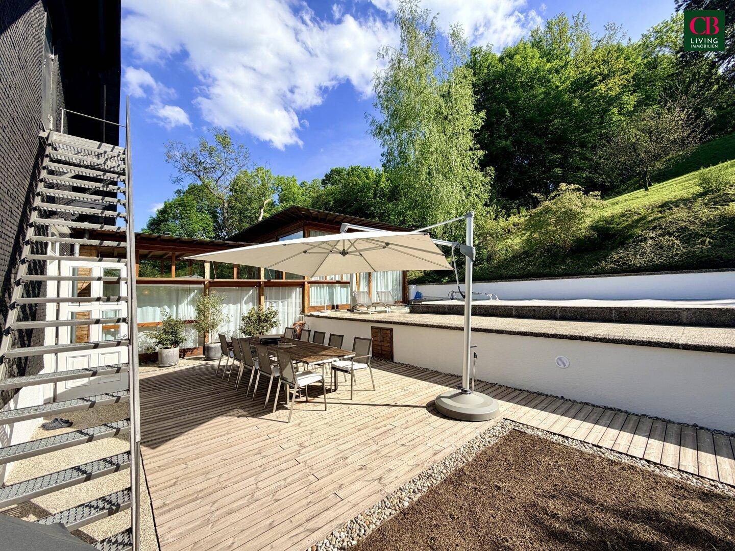 Große Holzterrasse mit Esstisch und Sonnenschirm, ideal für Mahlzeiten im Freien.