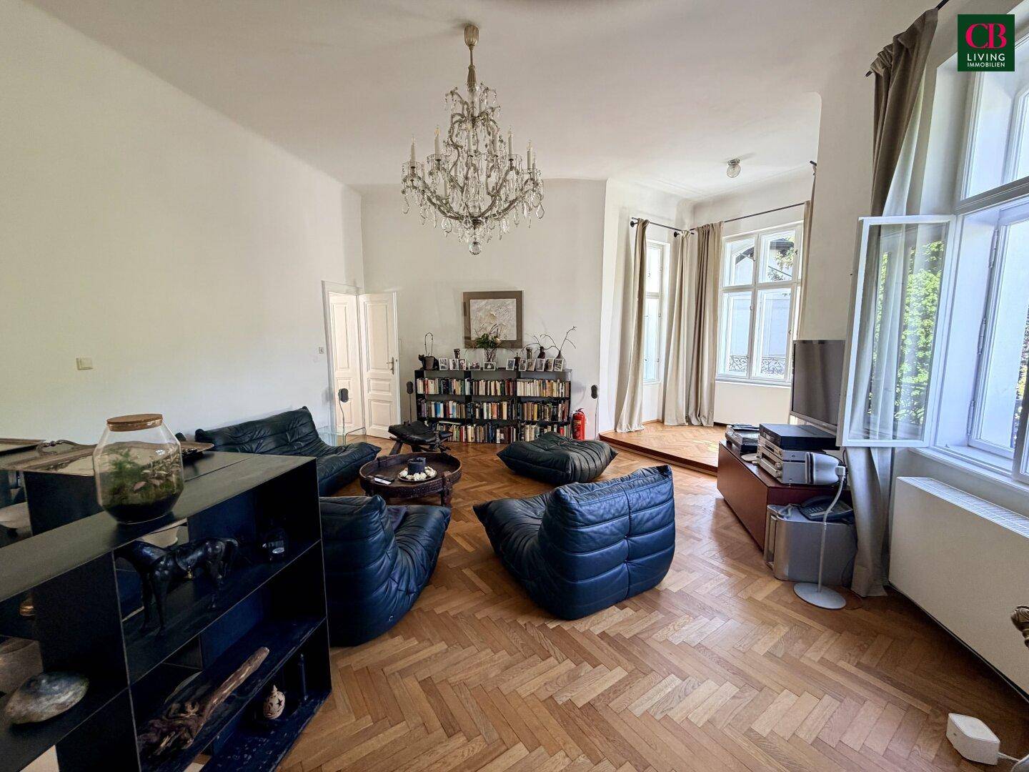 Großzügiges Wohnzimmer mit Fischgrätparkett, bequemen Sitzmöbeln und einem eleganten Kronleuchter.