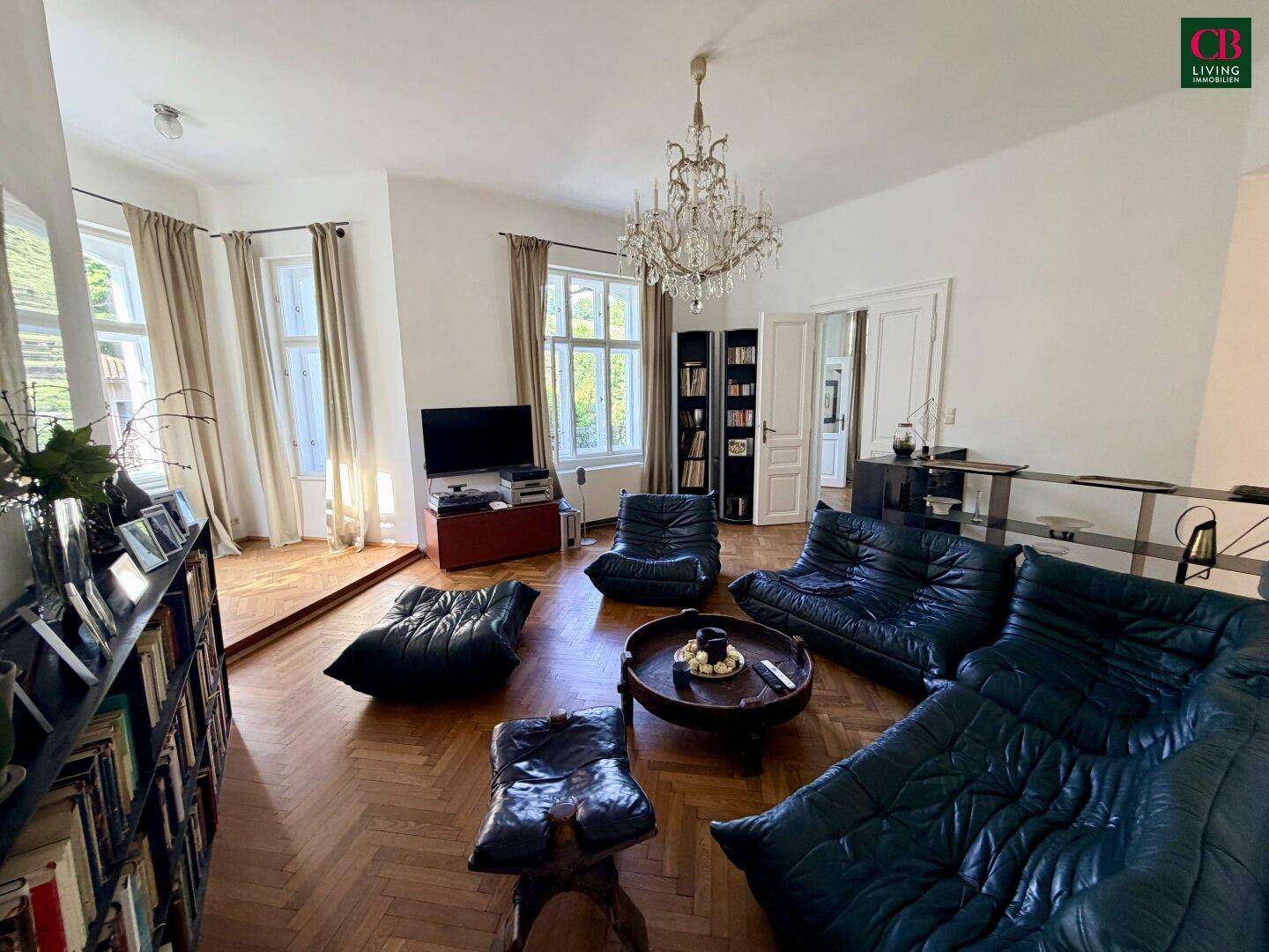 Helles Wohnzimmer mit dunklen Ledersofas, Bücherregalen und großen Fenstern mit Blick nach draußen.