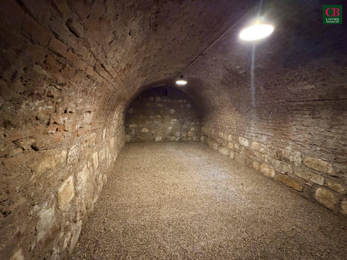 Historischer Gewölbekeller mit unverputzten Ziegelwänden und Kiesboden, ideal zur Lagerung.