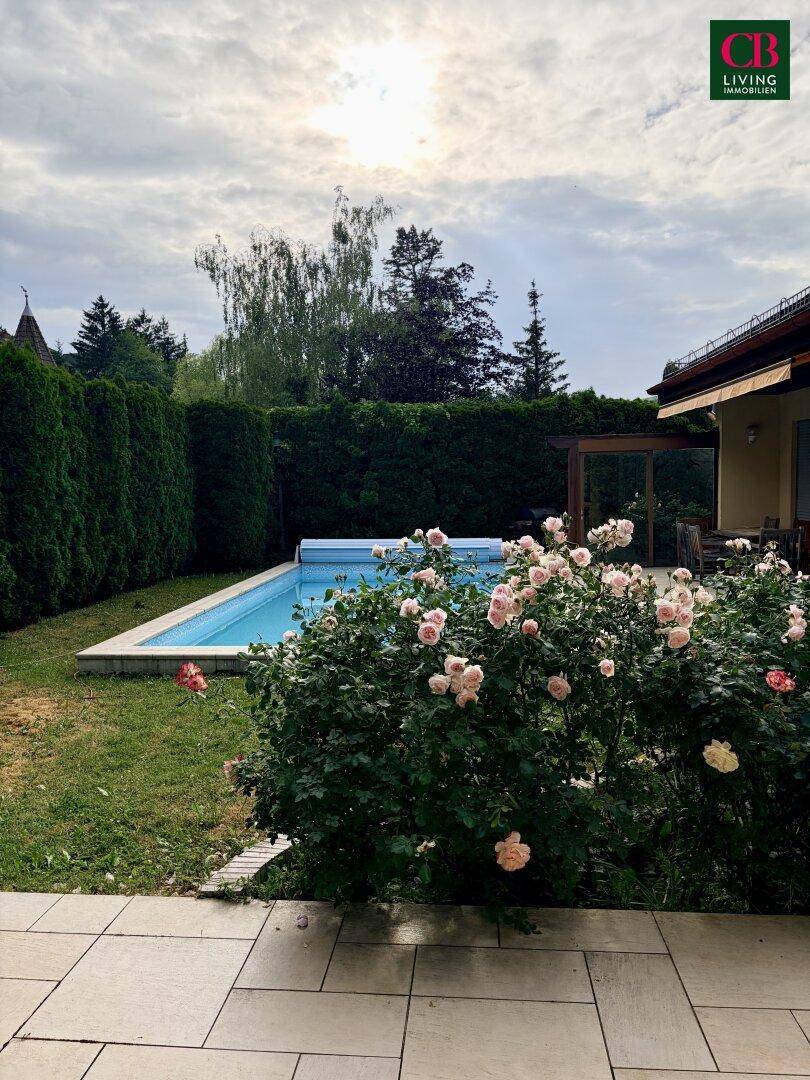 Gartenbereich mit Pool, gepflegtem Rasen und blühenden Rosen unter einem bewölkten Himmel.