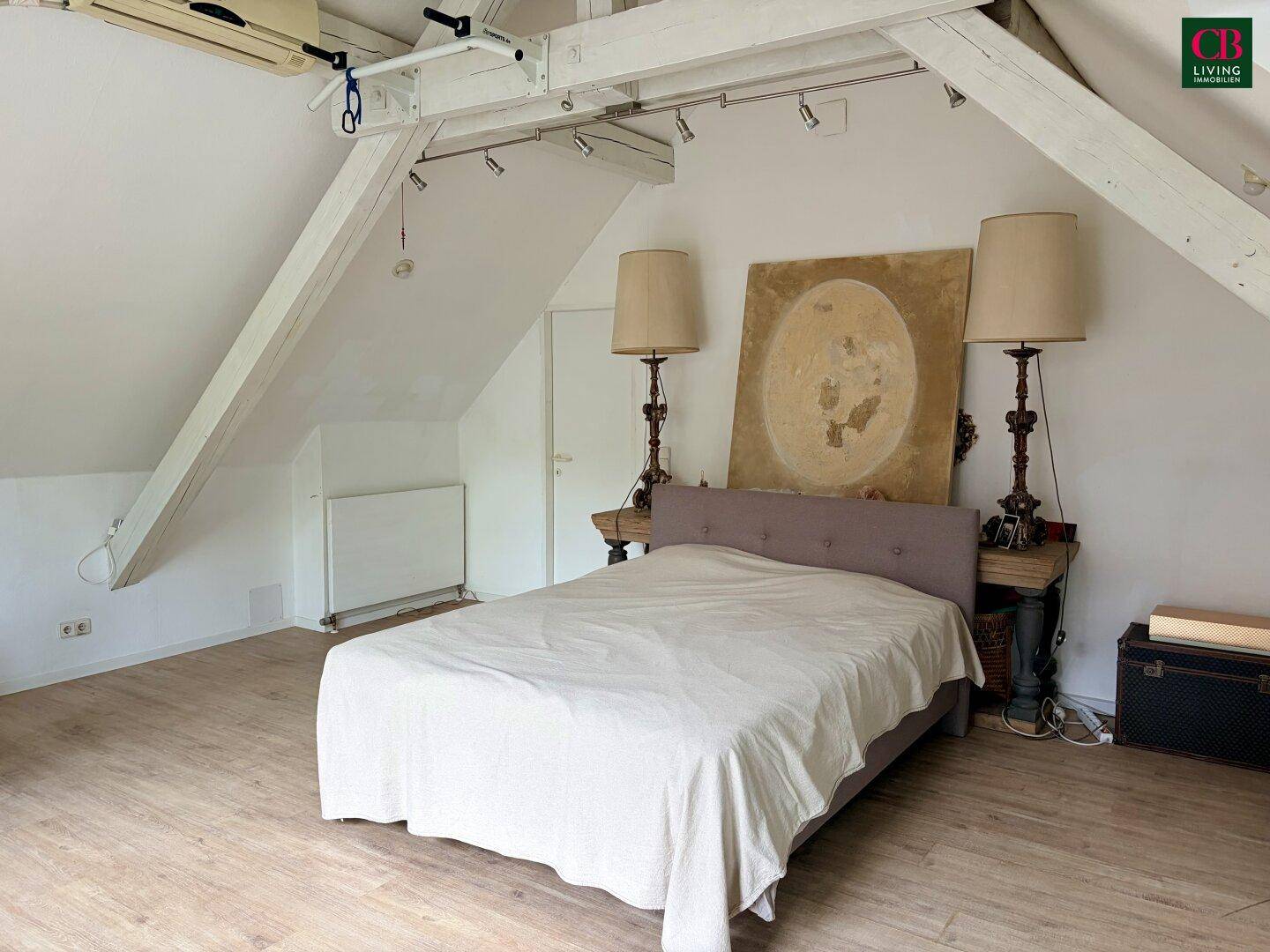 Helles Schlafzimmer im Dachgeschoss mit Holzbalken, Holzboden und einem großen Doppelbett.