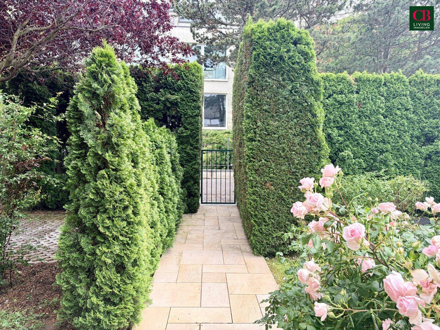 Gepflegter Gartenweg mit hohen Hecken und blühenden Rosen, der zu einem Tor führt.