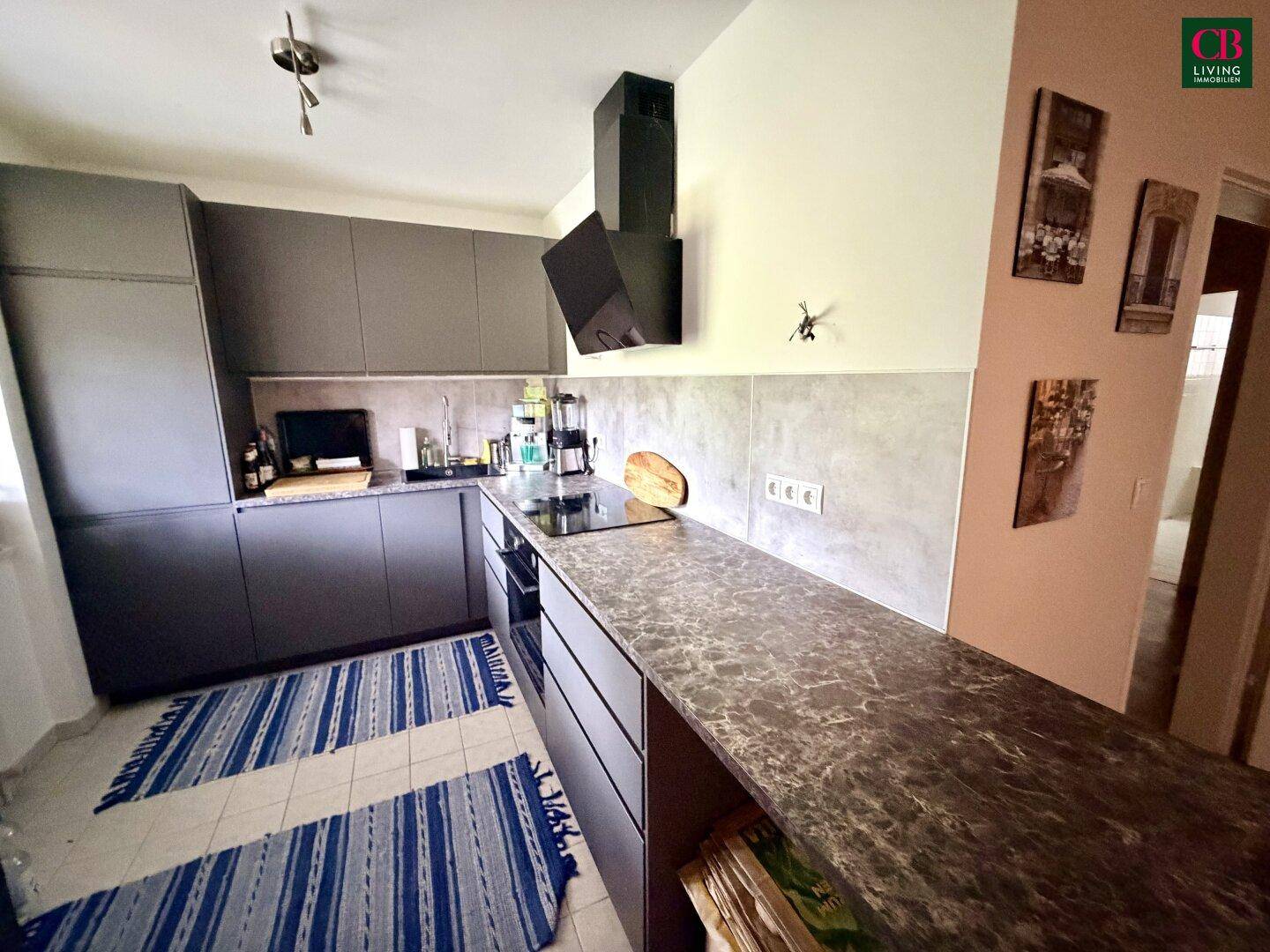Moderne Küche mit grauen Schränken, dunkler Arbeitsplatte und Induktionskochfeld.