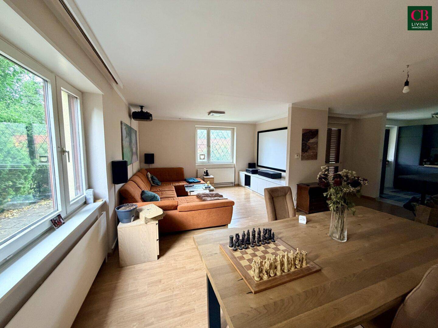 Geräumiger Wohn-Essbereich mit Holzboden, großer Couch und Esstisch mit Schachspiel.