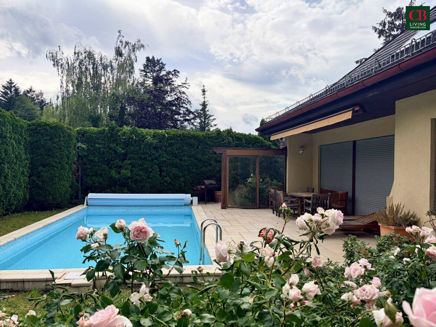 Außenbereich mit großem Pool, angrenzender Terrasse und blühenden Rosen im Garten.
