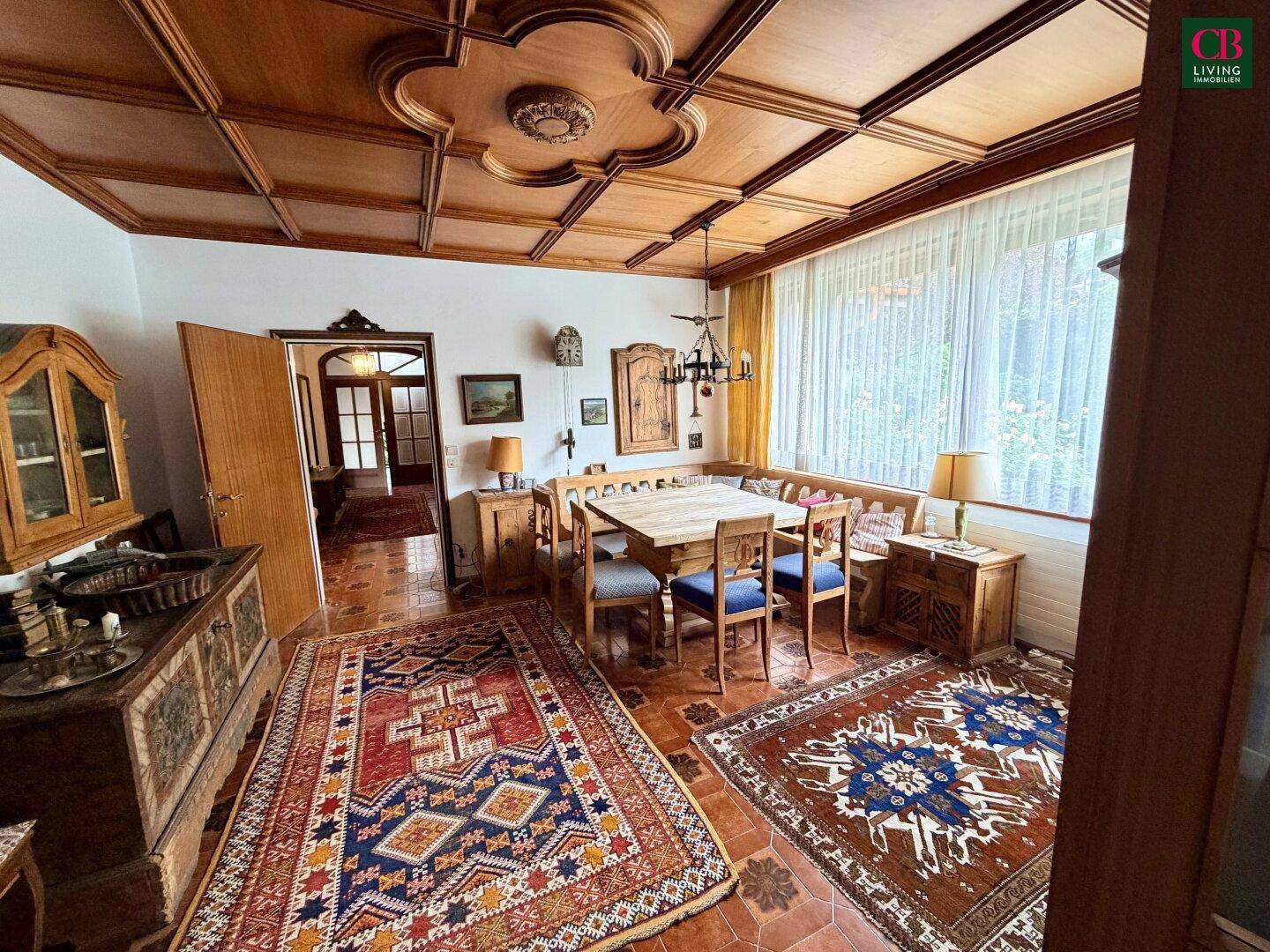 Gemütliches Esszimmer mit Holztäfelung an der Decke, großem Esstisch und traditionellen Teppichen.