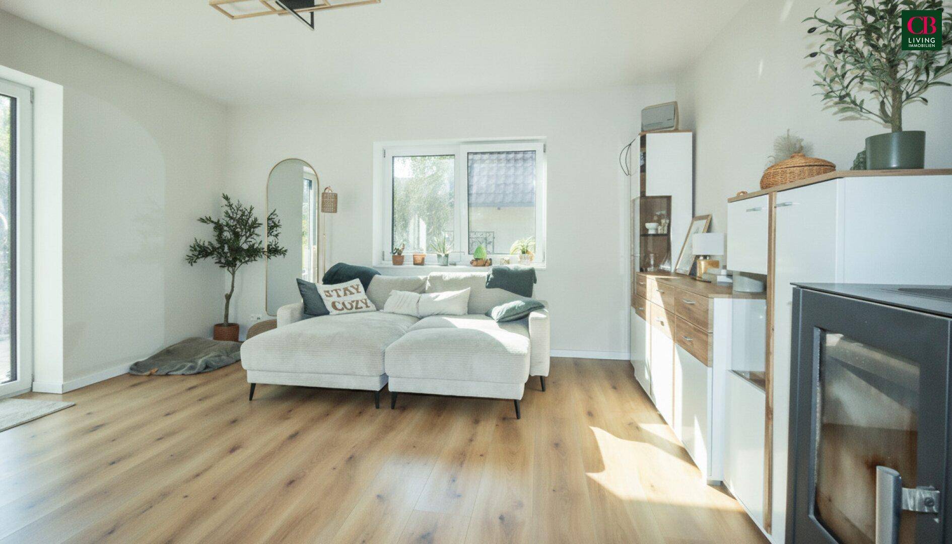 Helles Wohnzimmer mit beigem Sofa, Holzboden und gemütlichem Kaminofen.