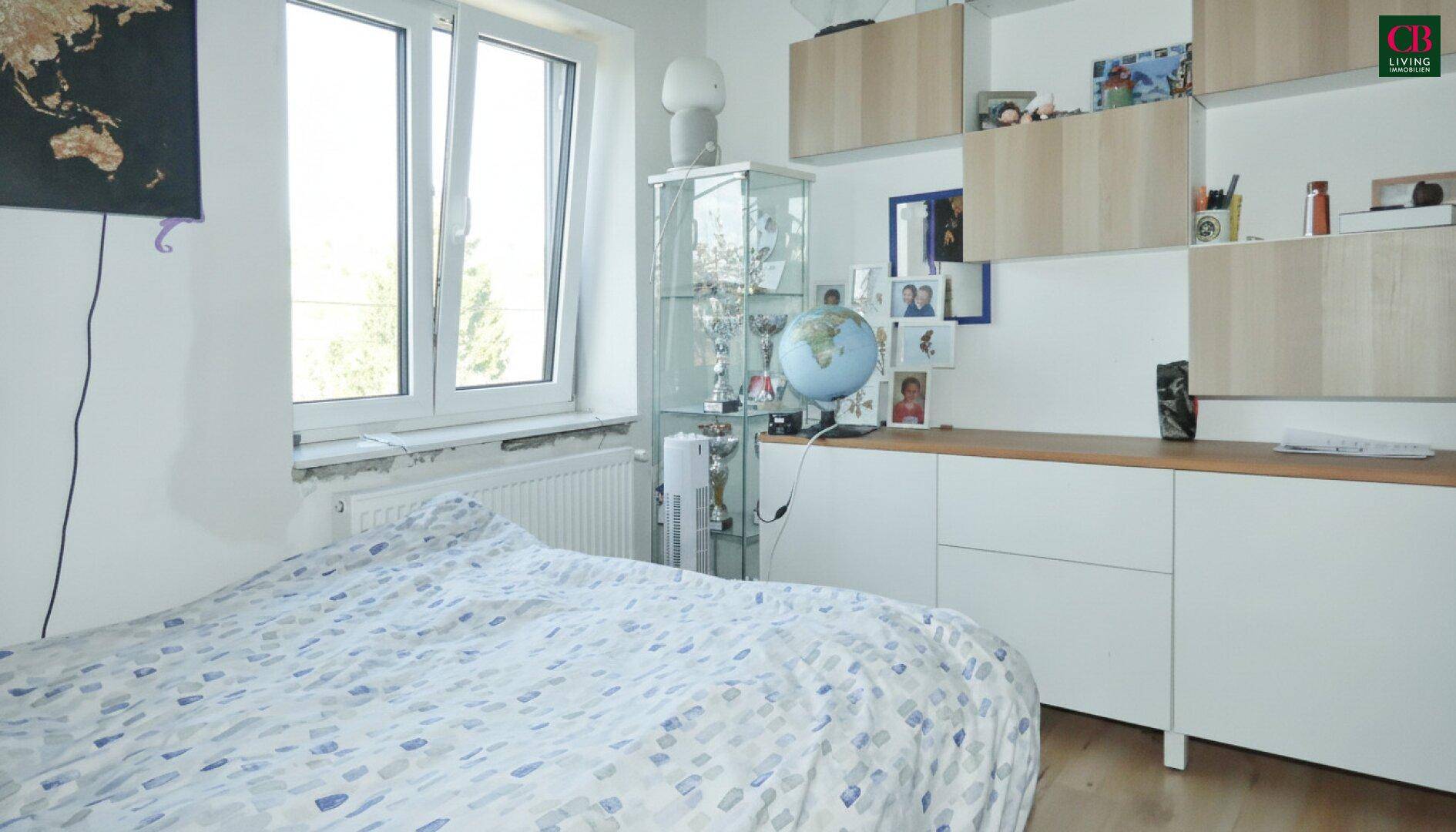 Schlafzimmer mit hellem Holzboden, großem Fenster und praktischen Schränken.