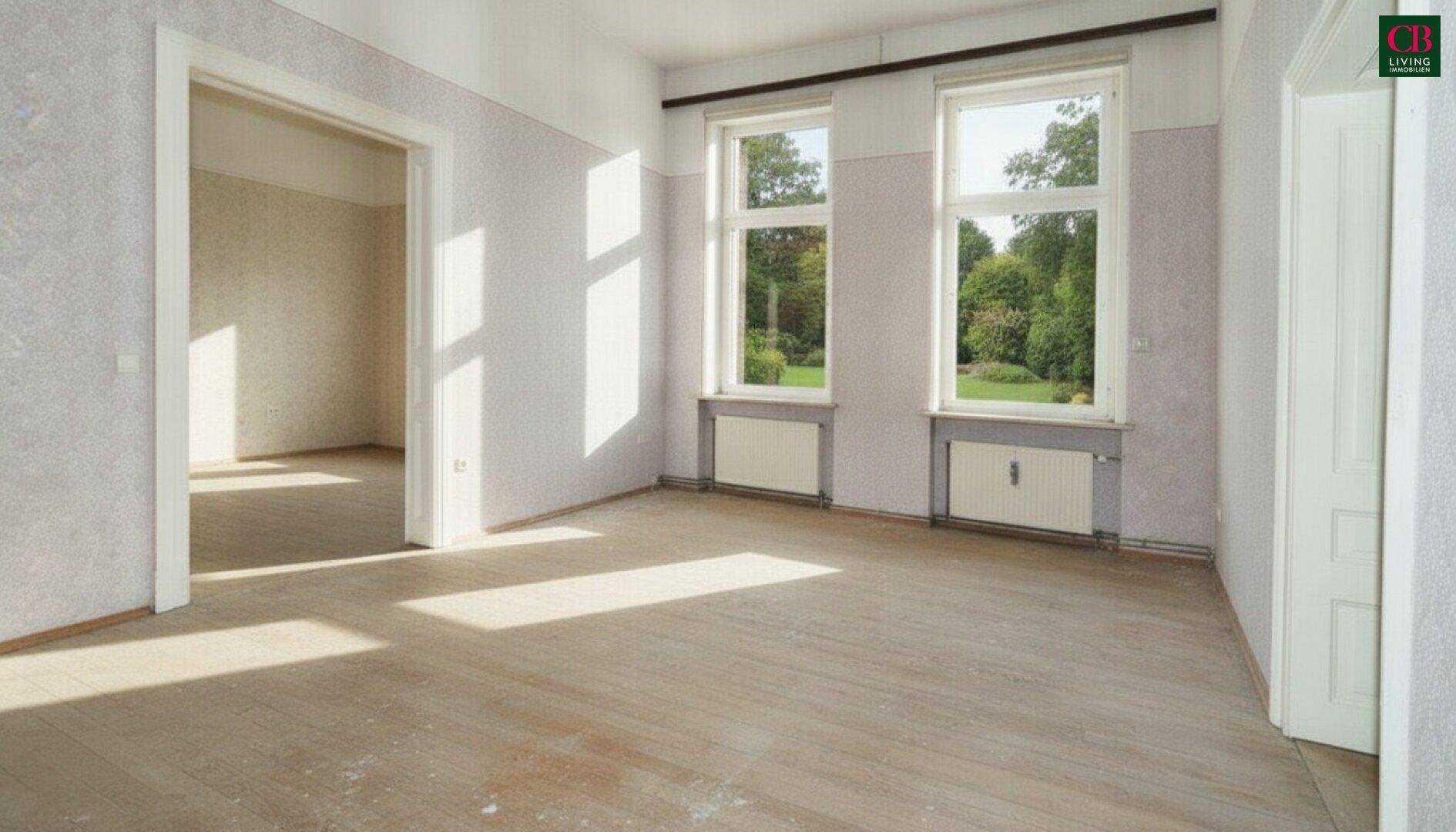 Heller, leerer Raum mit Holzboden und großen Fenstern, die viel Tageslicht hereinlassen.